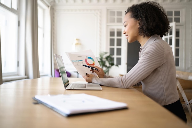 A person sitting at a desk, reviewing financial documents and using a spreadsheet on their laptop to analyze their income and expenses.