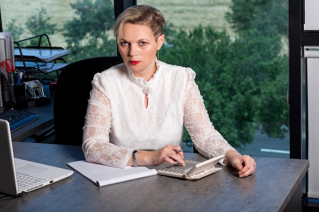 A woman sitting at her desk, reviewing financial documents and using a calculator. She looks focused and confident.