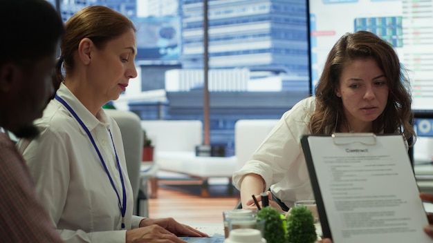 A doctor consulting with a patient, reviewing medical documents, with the insurance agent in the background.
