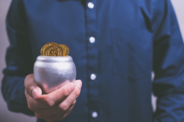 A close-up shot of a hand placing coins into a piggy bank, with rays of light shining on the coins. The scene evokes feelings of growth, savings and security.