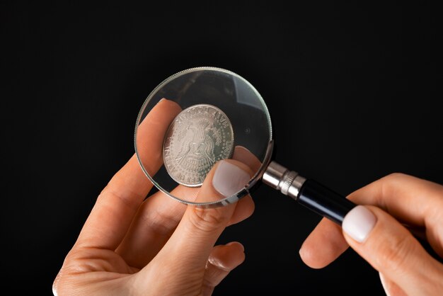 A hand using a magnifying glass to examine a stock certificate closely indicating the need for diligence and research when investing in penny stocks. The certificate contains small print.