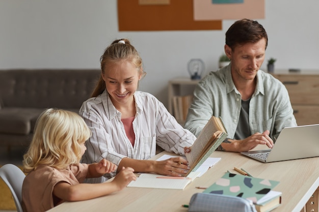 A family of four sitting at a table, reviewing documents and using a laptop, with a calculator and notebooks in the background, illustrating the planning and financial considerations involved in saving for education.