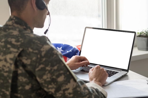 A US military service member sitting at a desk, focused on a laptop screen displaying an online course application form. The setting is a quiet study area.