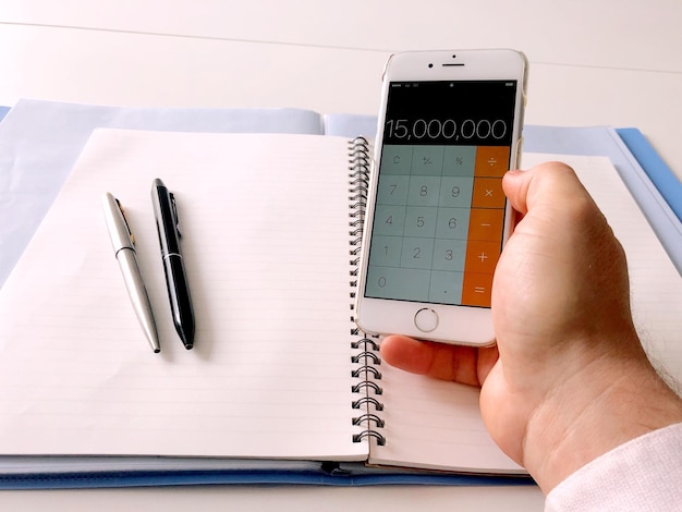 Hand holding a smartphone displaying a student loan repayment calculator app, with various data entry fields visible on the screen.