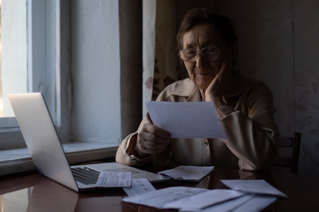 Close-up of a person looking stressed while reviewing financial documents on their desk at home, with bills and a calculator visible. The lighting is soft, creating a serious and concerned mood.