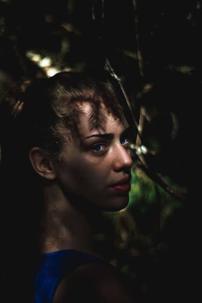 A close-up of Saga Anderson's face, looking determined and focused. She is holding a flashlight and the background shows a dark, foreboding forest.